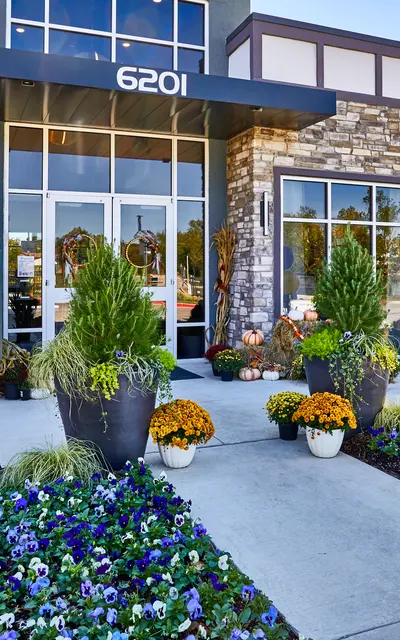 Front view of a modern leasing center with stone accents and a sign. Flowers and plants decorate the entrance, with balloons in the background.