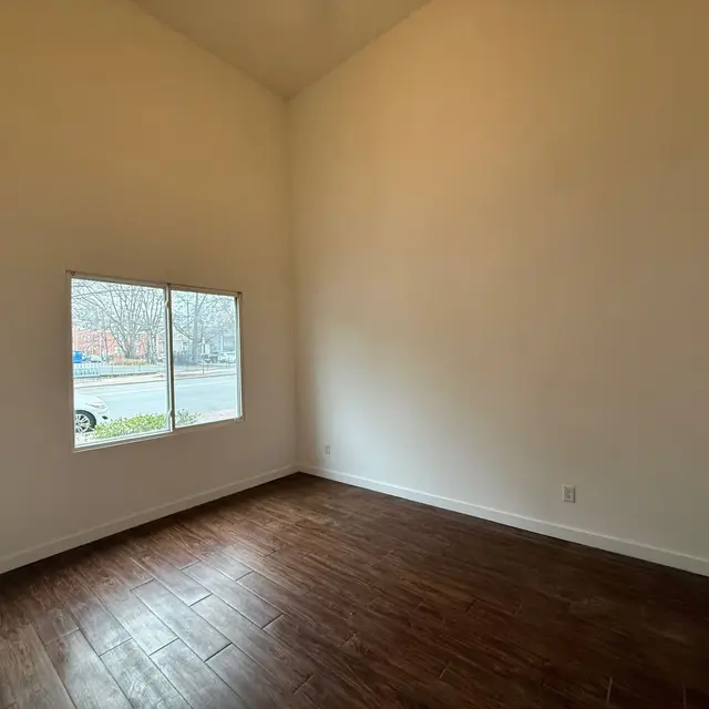 An empty room with wooden flooring and a large window.