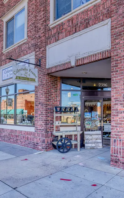 A brick building with large windows, featuring storefronts and a sidewalk with flower pots.