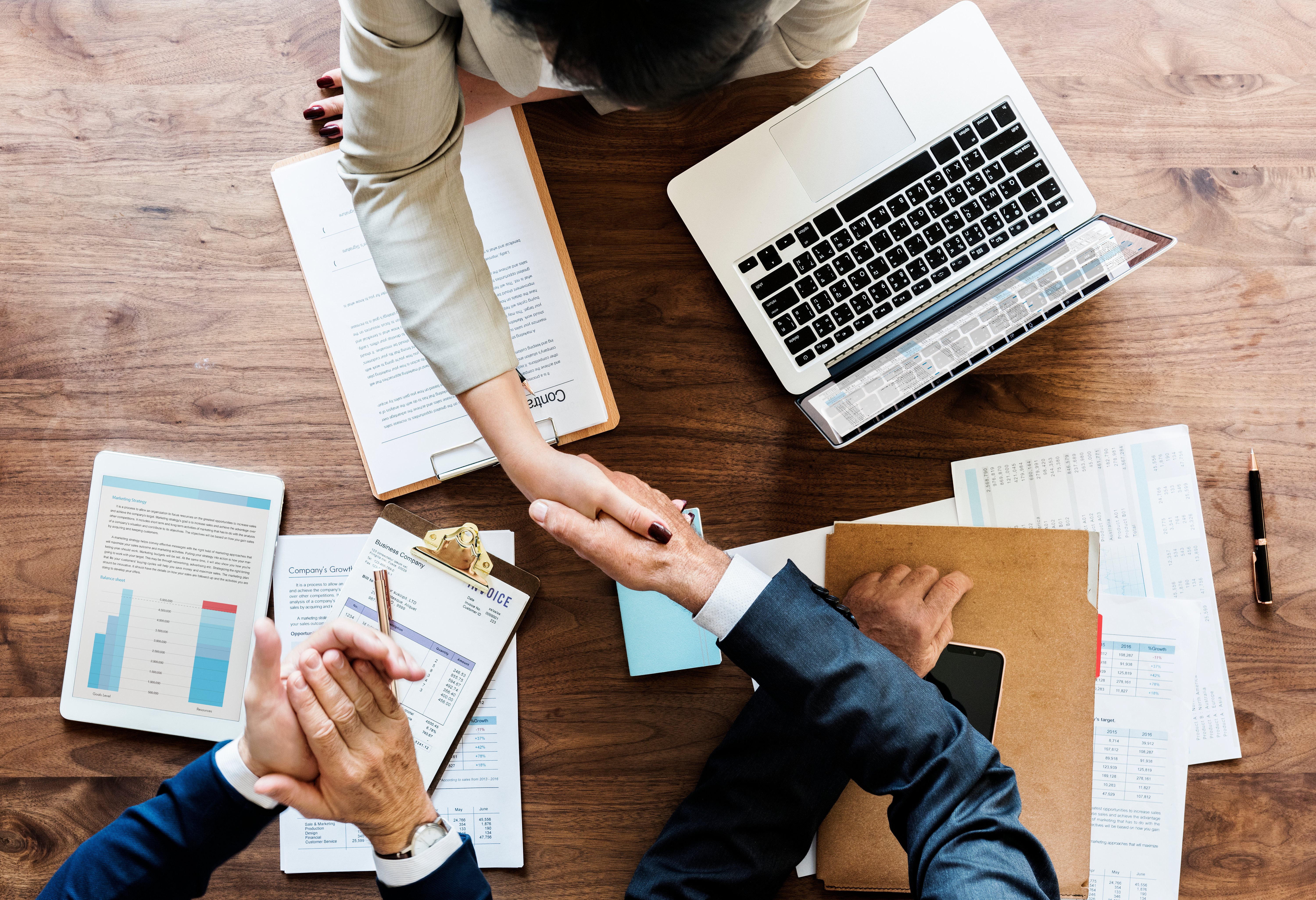 Successful Business Agreement Above view of a business meeting with hands shaking over a table filled with documents, a laptop, and stationery