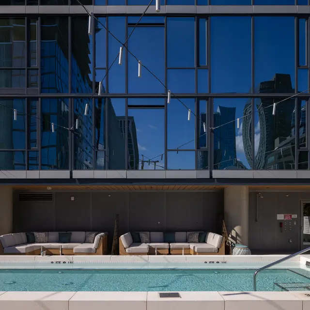 A sleek outdoor pool with a clean, modern design situated in front of a large glass building. The water is clear, and there are comfortable loungers nearby. The building's reflections can be seen in the glass facade.