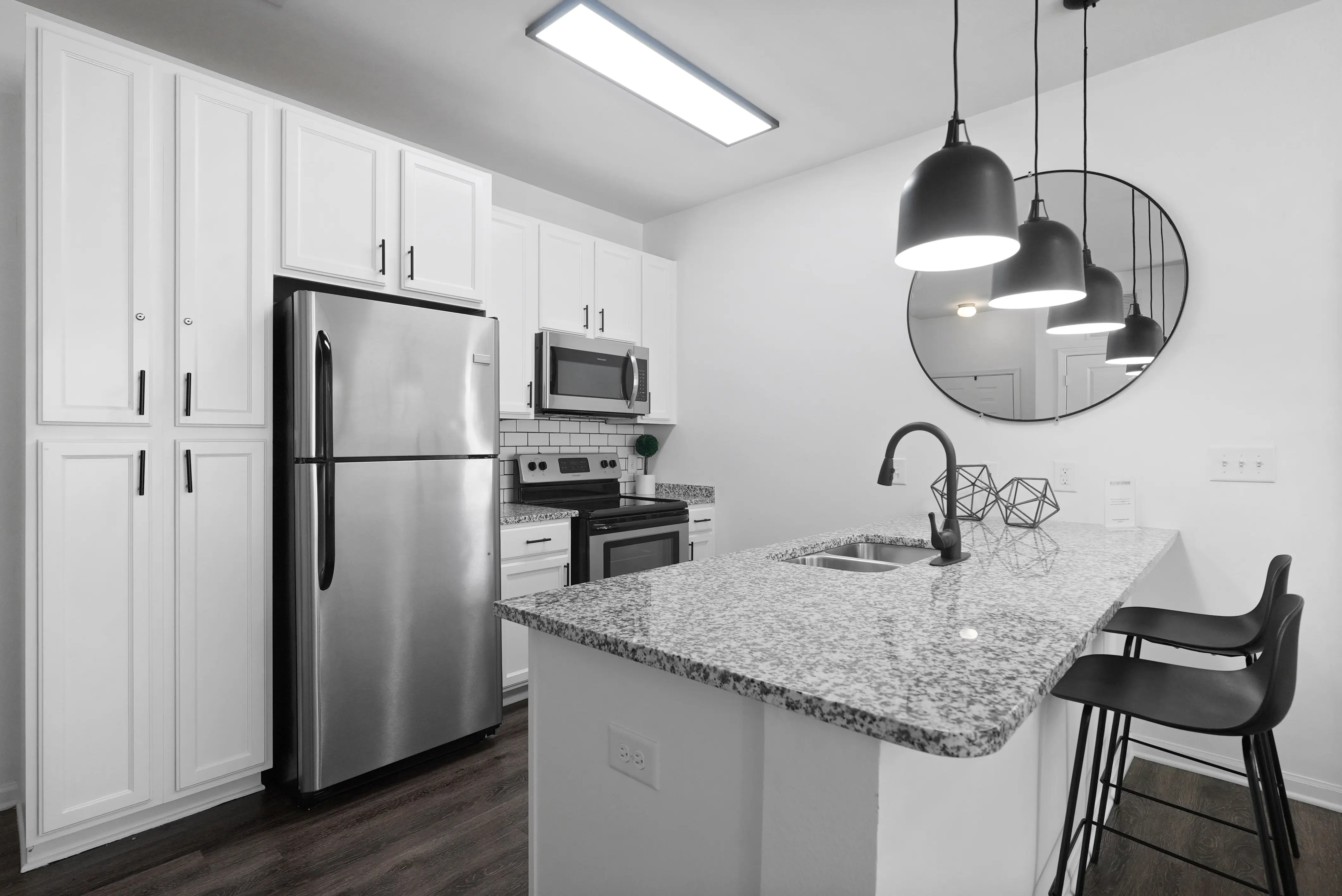A modern kitchen featuring white cabinetry, stainless steel appliances, and a granite countertop island with bar stools.