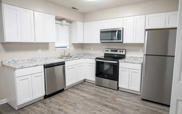 Summit at 501 Modern kitchen featuring stainless steel appliances, white cabinets, granite countertops, and hardwood floors. Bright and spacious layout.