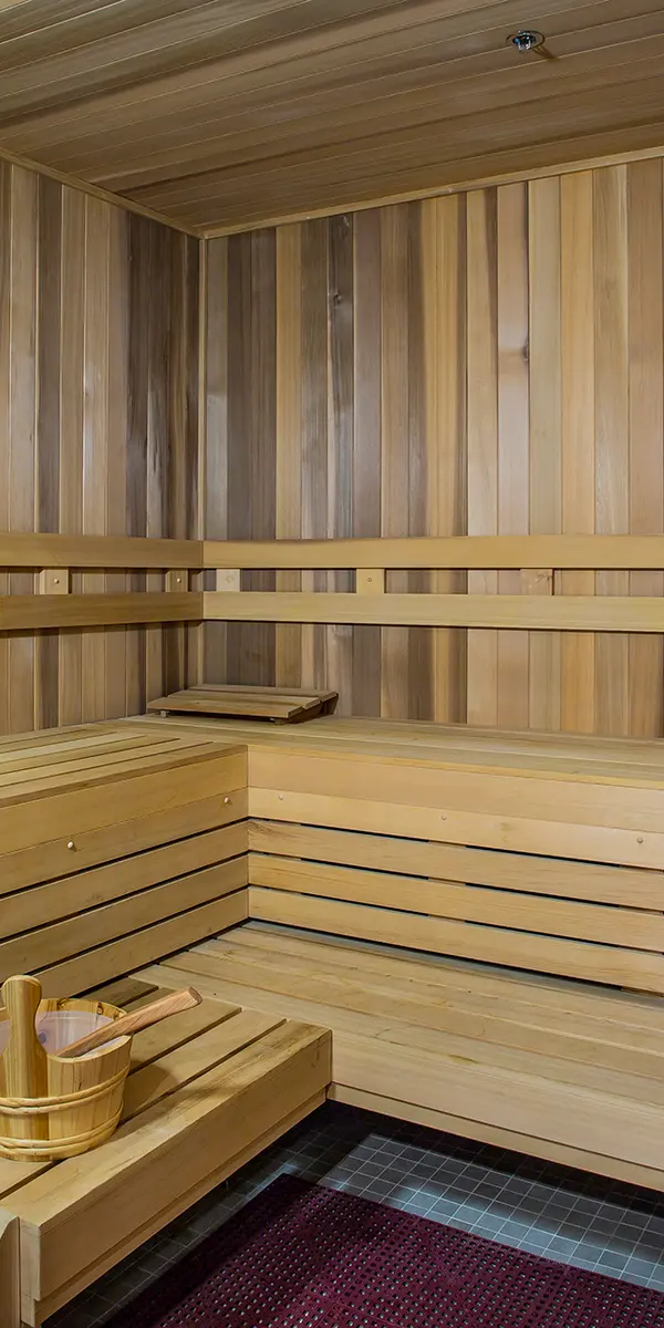 A wooden sauna interior with benches, a small table, and a bucket, featuring warm, natural wood tones and a cozy atmosphere.