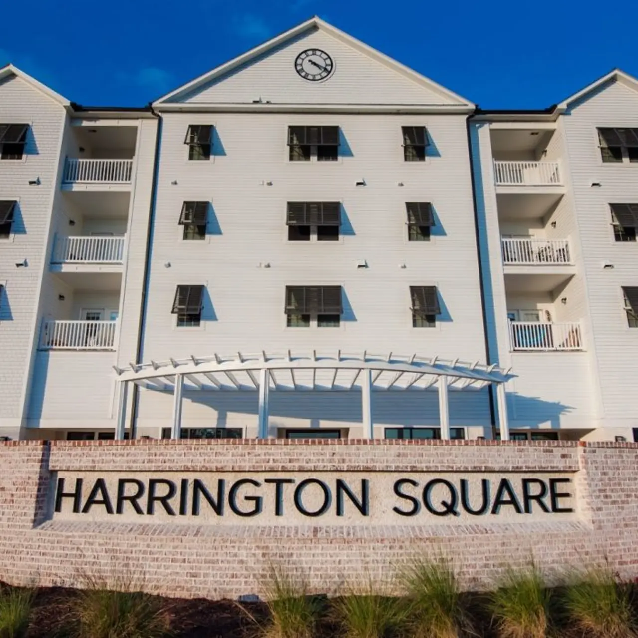Harrington Square Building Exterior Exterior view of Harrington Square, a multi-story building featuring white walls and balconies, with palm trees and a sign at the front.