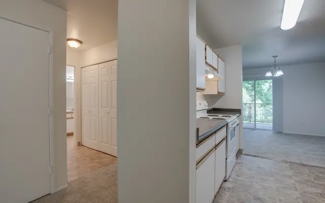 View of a small kitchen area leading into a living space with a door and hallway visible on the left