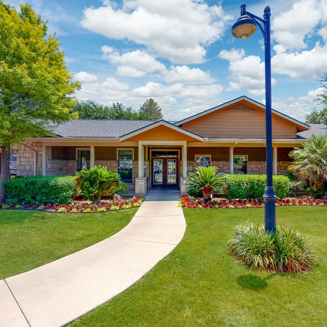 A modern house with a stone and wood exterior, surrounded by lush green landscaping and trees under a blue sky with fluffy clouds.