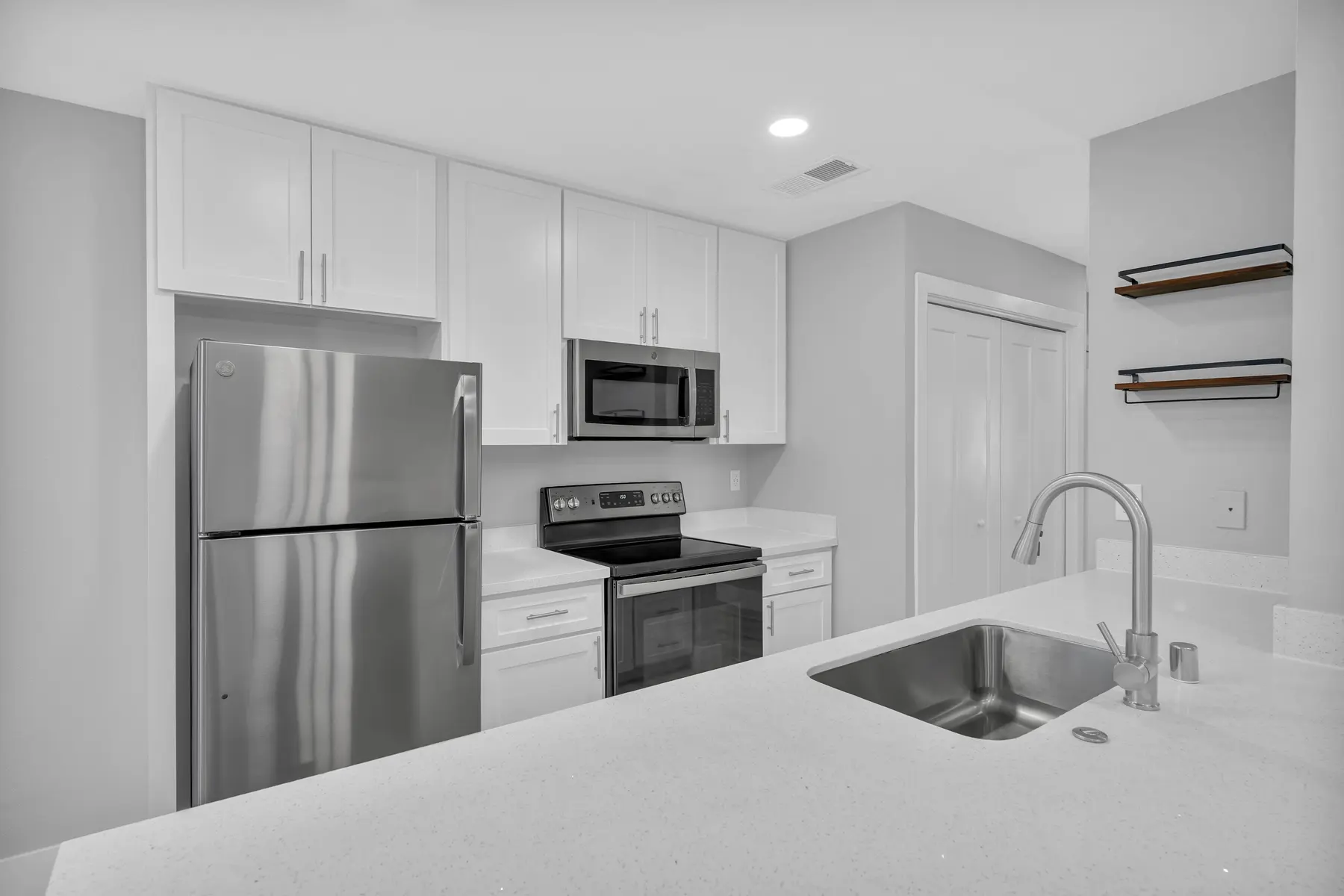A sleek modern kitchen featuring a stainless steel refrigerator, a microwave, and an oven, complemented by white cabinetry and a quartz countertop with a sink.