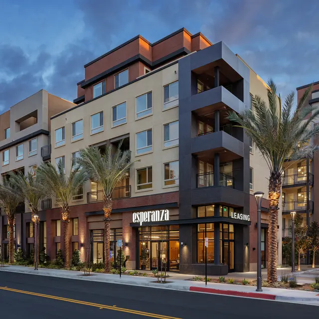 Modern apartment building exterior with palm trees on the side, featuring a leasing office at dusk.