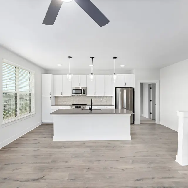 Modern Kitchen Interior A spacious modern kitchen with white cabinetry, stainless steel appliances, and a large island in the center. The room features hardwood floors and large windows letting in natural light.