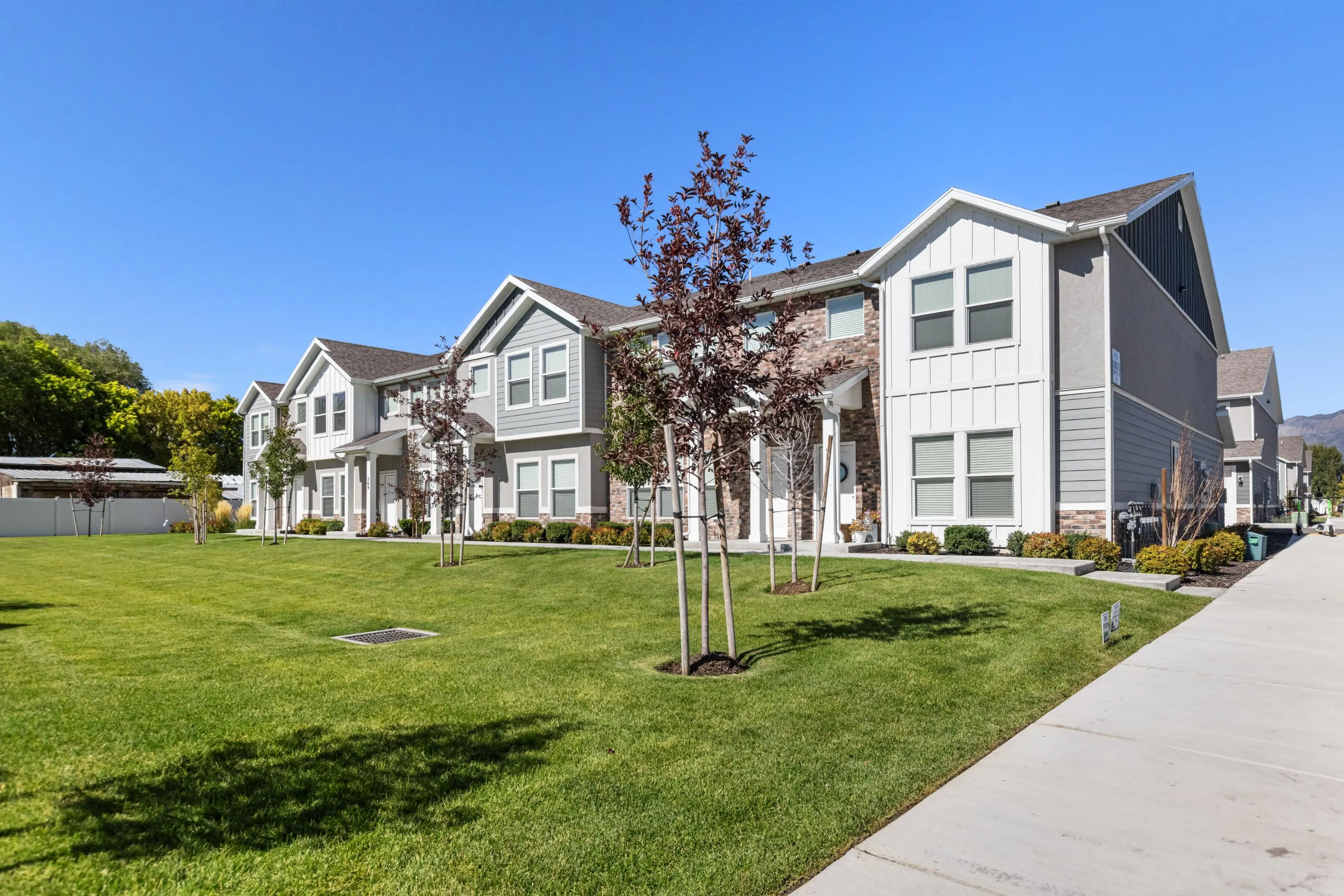 Modern Townhouses with Green Space A row of modern townhouses with a well-maintained lawn and trees, under a clear blue sky.