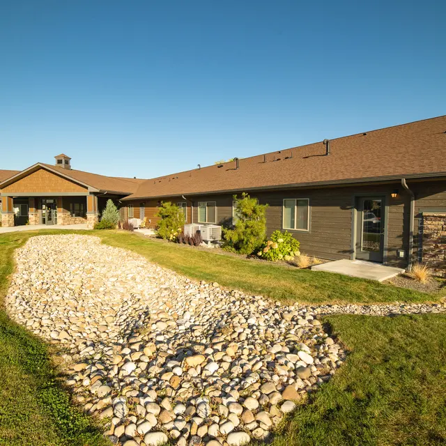 Building Exterior with Stone Path Exterior view of a single-story building with a landscaped path made of stones and well-maintained grass under a clear blue sky.