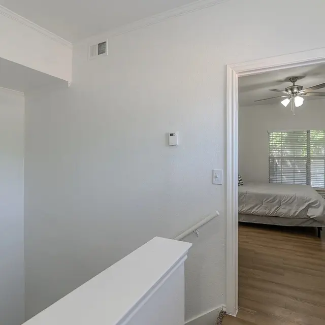 A bright and clean interior hallway leading to a bedroom, featuring light-colored walls and wooden flooring.