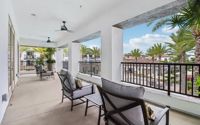 A modern balcony with comfortable seating and a view of palm trees and a pool area