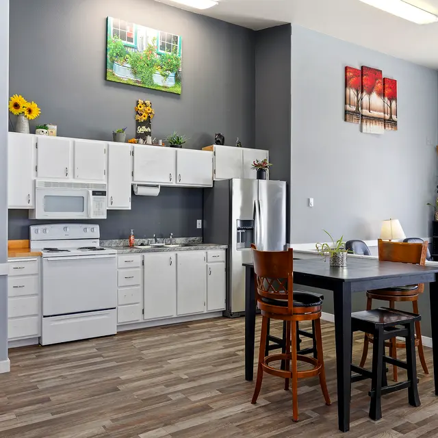 Modern Kitchen Design A modern kitchen featuring white cabinets, a microwave, a stove, and a dining table with high stools. The walls are painted in light gray and dark gray, adorned with small plants and framed pictures.