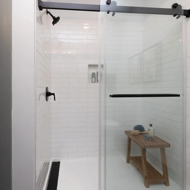 A modern shower stall with clear glass doors and a wooden bench inside, featuring white tiled walls.