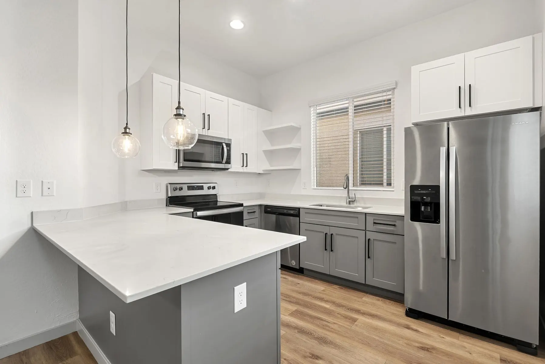 Modern kitchen with gray and white cabinetry, stainless steel appliances, and pendant lighting over an island.
