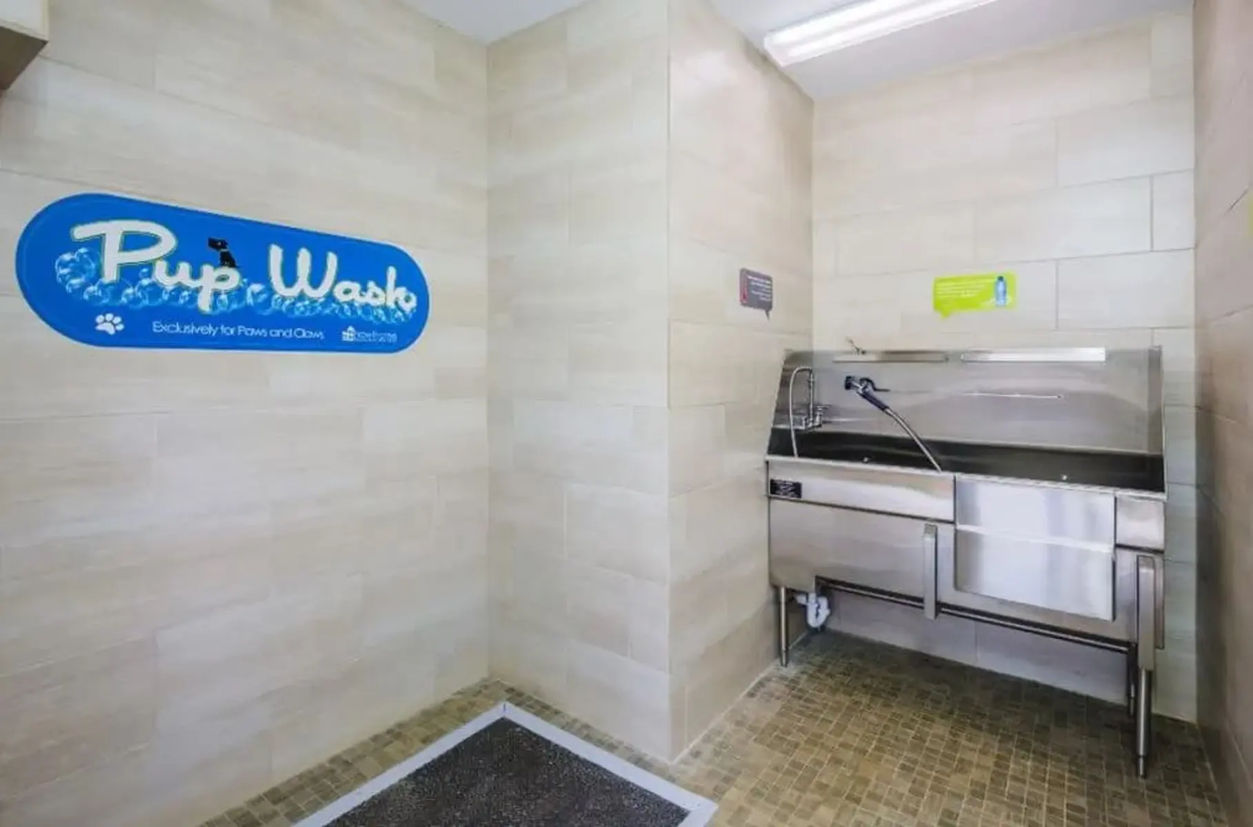 A pet washing station with tiled walls and a stainless steel wash basin. The sign reads 'Pup Wash'.