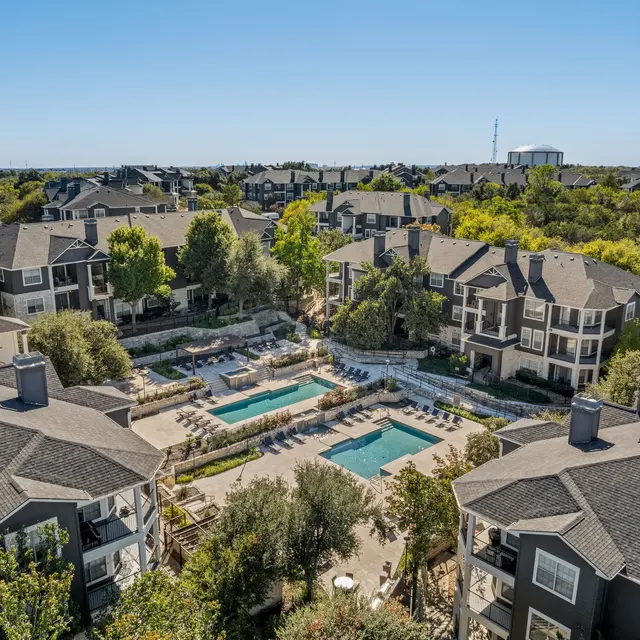 An aerial view of a residential apartment complex with two swimming pools surrounded by trees and landscaped gardens.