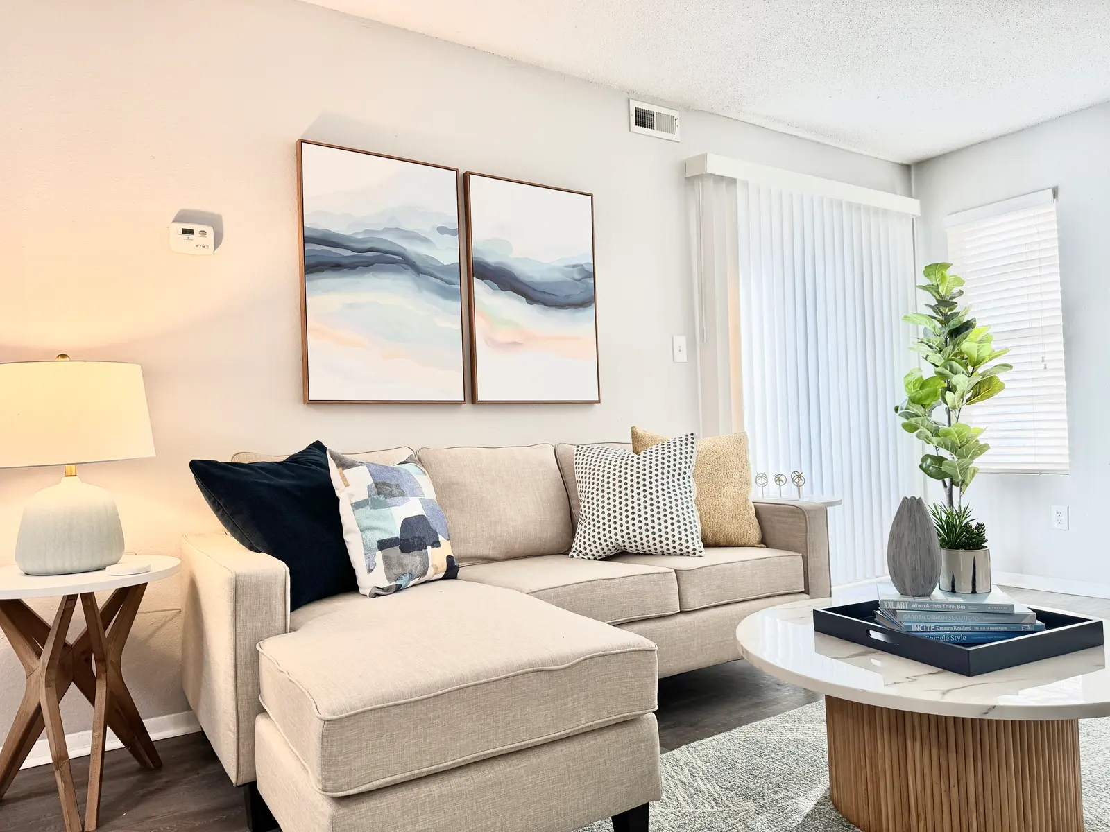 A modern living room with a beige sofa, decorative cushions, a round coffee table, and wall art.