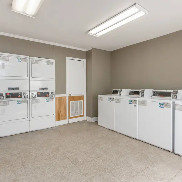 A clean laundry room featuring multiple washing machines and dryers arranged against the walls, with a door leading to another area.