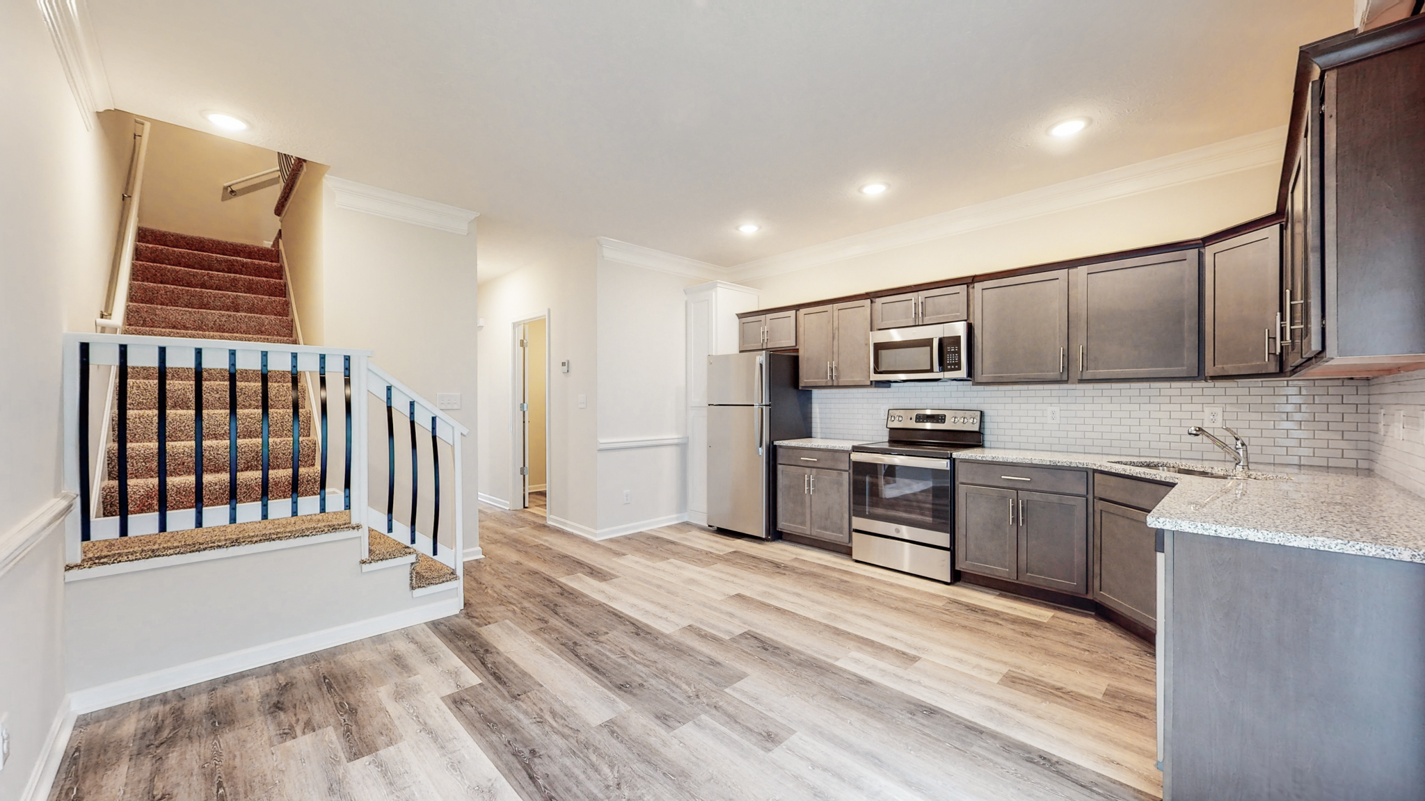 Modern Kitchen and Living Space View of a modern kitchen and living area featuring dark cabinetry and stainless steel appliances, with stairs leading to an upper level.