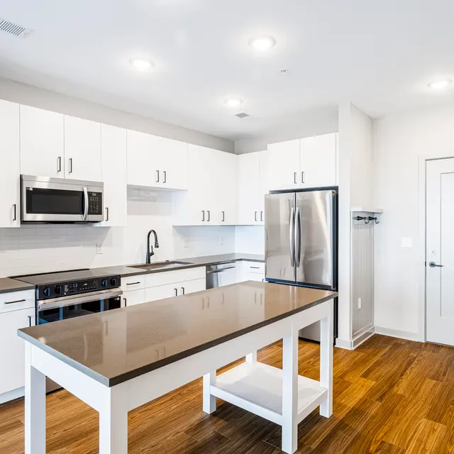 A bright and modern kitchen featuring white cabinetry, stainless steel appliances, and a large central island with a dark countertop.