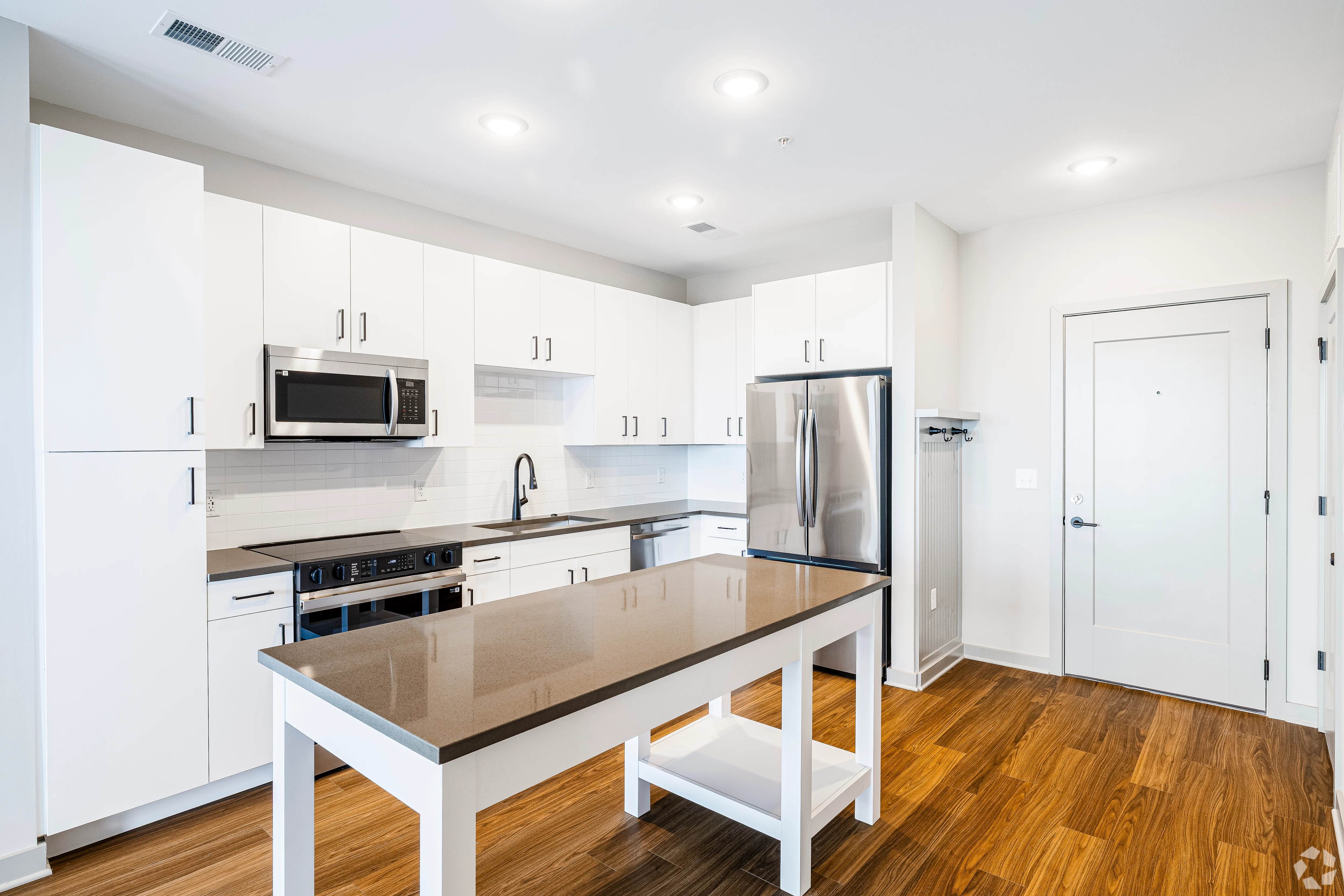 A bright and modern kitchen featuring white cabinetry, stainless steel appliances, and a large central island with a dark countertop.