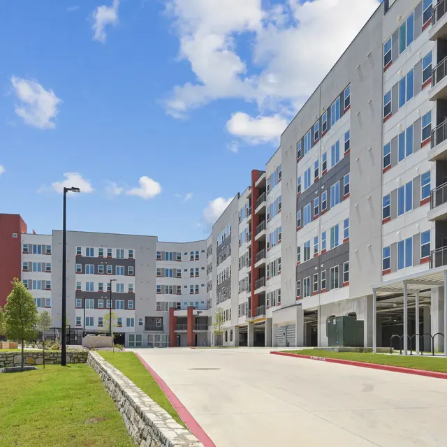 A modern multi-story apartment building with a landscaped area in the foreground and a clear blue sky.