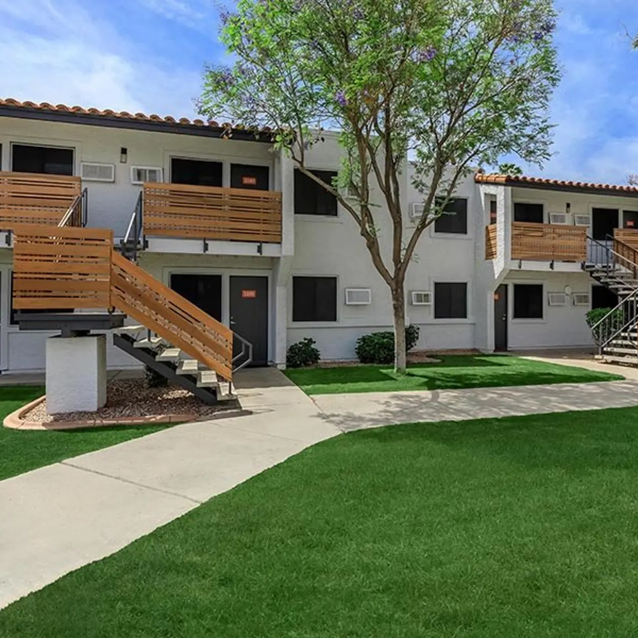 Exterior view of a two-story apartment complex with wooden staircases and green lawn.