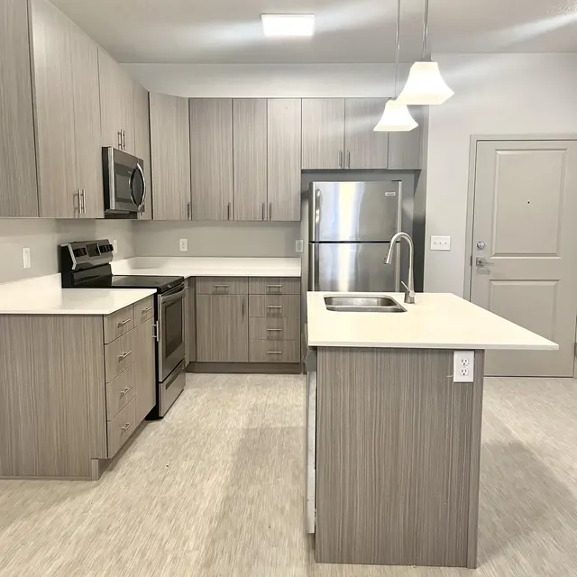 A modern kitchen featuring light gray cabinetry, stainless steel appliances, and a large island with a sink.