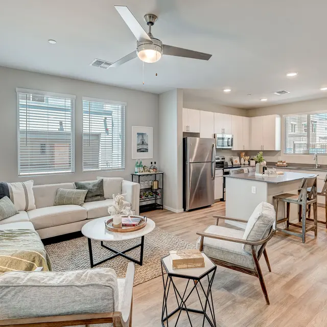 Modern Open-Concept Living Space A modern open-concept living room and kitchen featuring a light-colored couch, circular coffee table, and seating area with stylish chairs. The kitchen has stainless steel appliances and a central island, all set in a well-lit space with large windows.