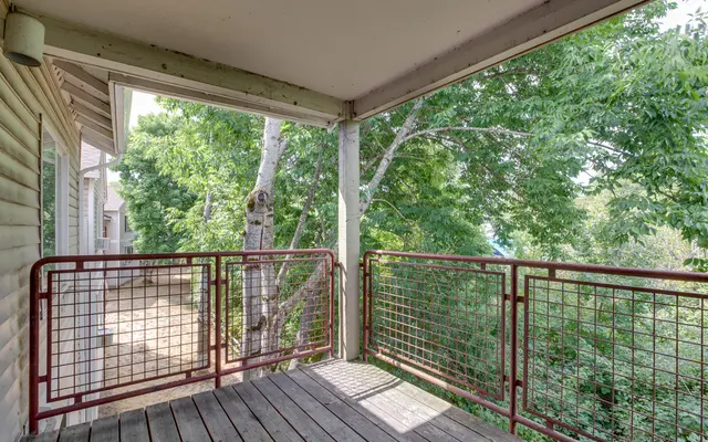 A view from a balcony with wooden flooring and a metal railing, surrounded by greenery.