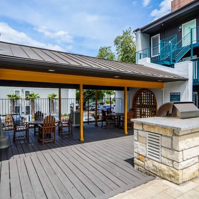 Outdoor Gathering Area An outdoor gathering area featuring a covered pavilion with wooden tables and chairs, a stone BBQ grill, and lush greenery nearby.
