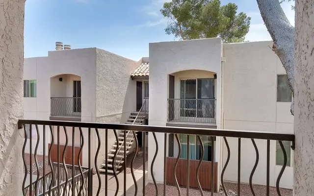 View from an apartment balcony showing two beige buildings with green lawns and trees.