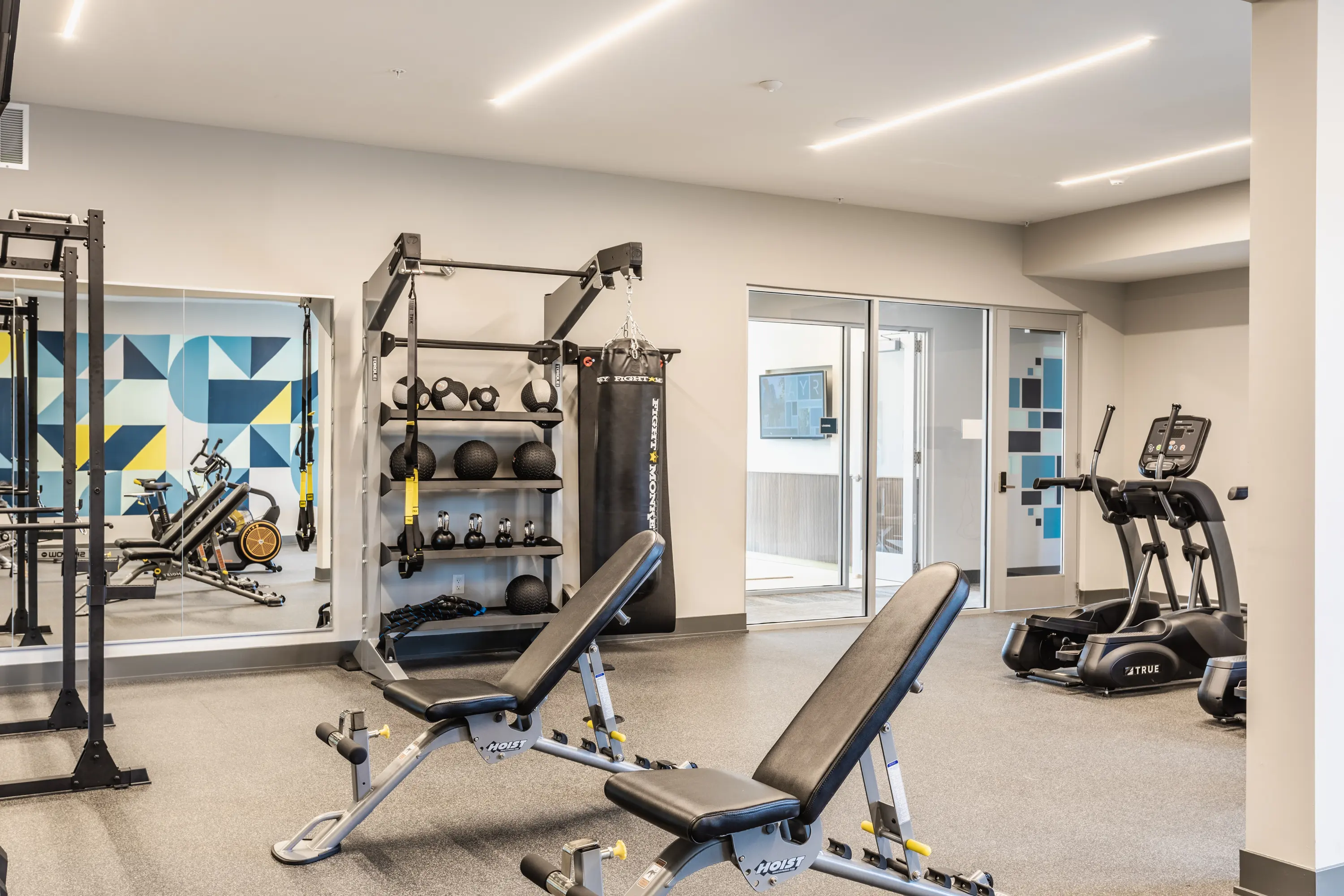 Modern Gym Interior Interior view of a modern gym featuring workout equipment including benches, weights, and cardio machines against a backdrop of geometric-patterned walls.