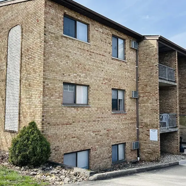 Brick Apartment Building A brick apartment building with multiple windows and balconies, surrounded by grass and a small landscaped area.