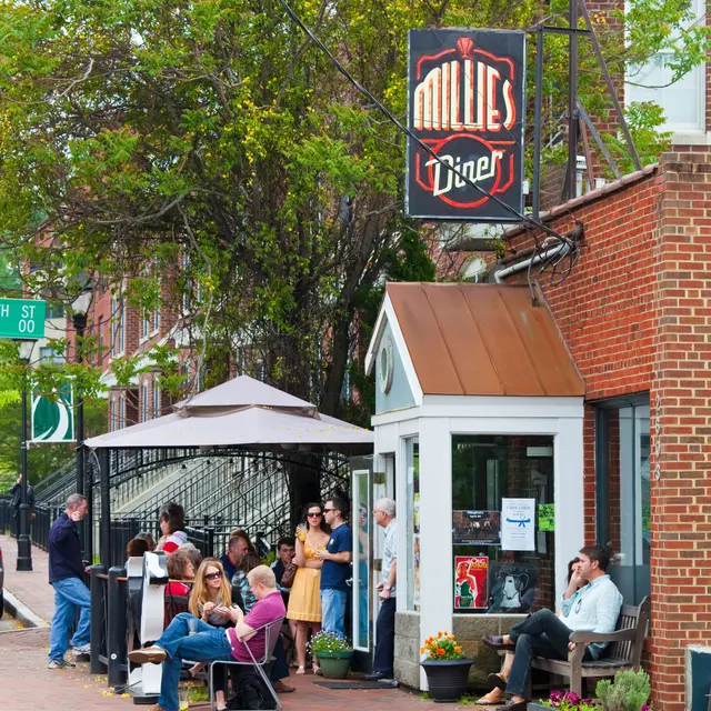 A street view of Millie's Diner in Carytown, VA with people seated outside and a green tree in the background.
