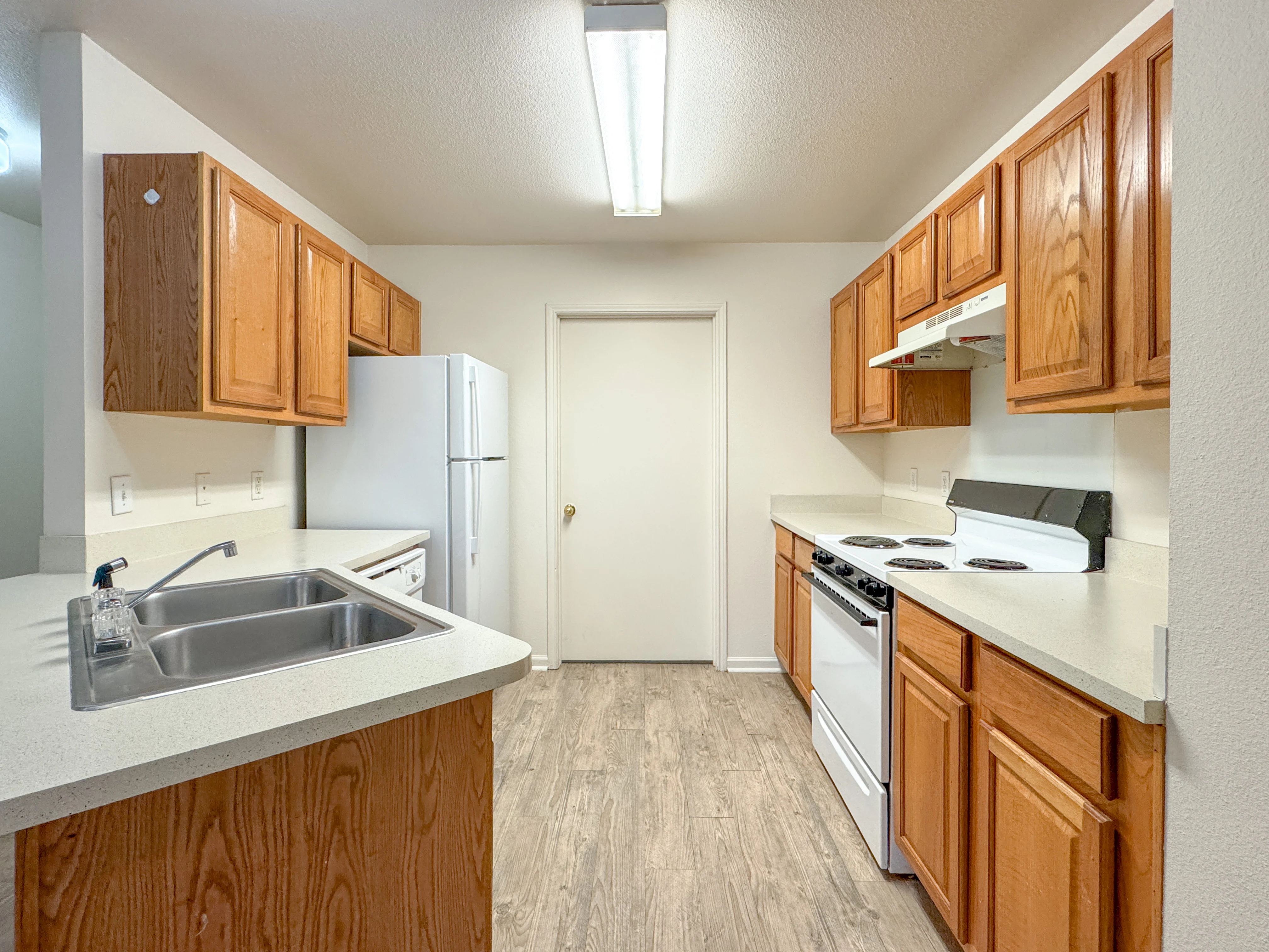 Modern Kitchen Interior A modern kitchen featuring wooden cabinets, a refrigerator, a stove, and a sink. The kitchen has a simple layout with white countertops and lighting from above.
