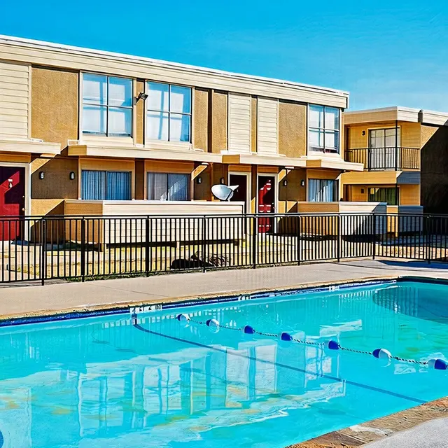 View of an outdoor swimming pool surrounded by an apartment complex with a clear blue sky.
