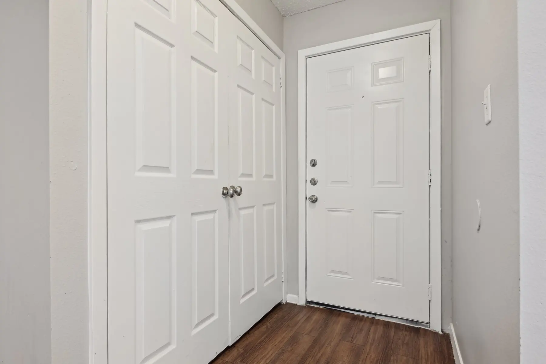 A view of a small entryway with two sets of white double closet doors and a white front door.