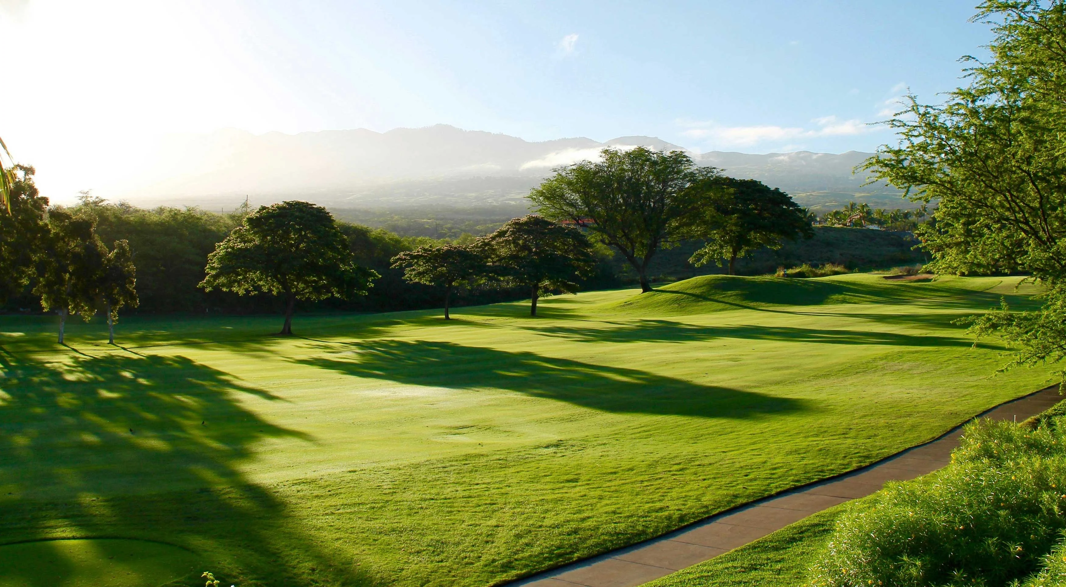 Beautiful Golf Course Scenery A picturesque golf course with lush green grass, trees, and mountains in the background under a clear blue sky.