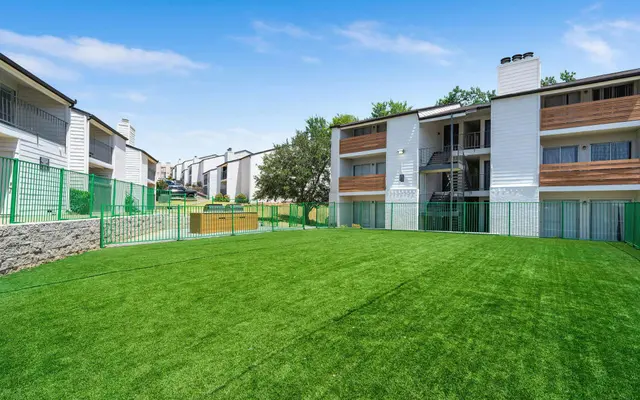 A spacious green lawn area surrounded by apartment buildings with balconies and green fencing.