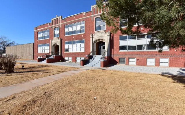 Historic School Building A historic brick school building with large windows and an entrance staircase, set against a clear blue sky and a grassy area.