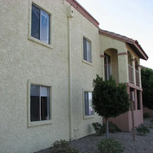Exterior of Apartment Building Exterior view of a beige apartment building with a stucco finish and shrubs in front.
