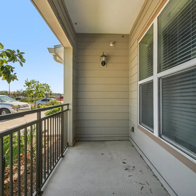 A view of a small patio area with a railing, featuring potted plants and a clear sky in the background.