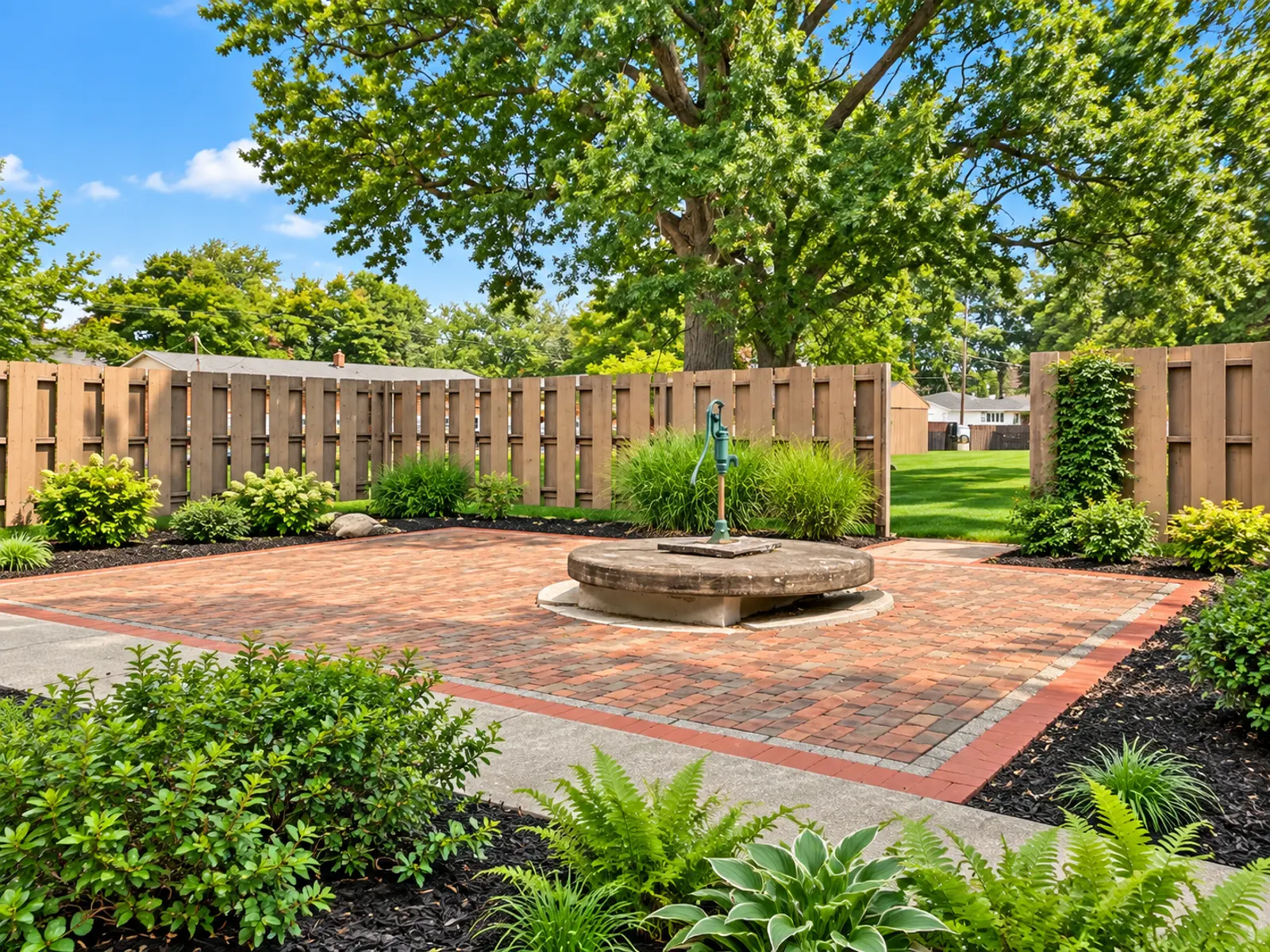 A landscaped outdoor garden area with a paved brick patio surrounded by greenery and wooden fencing.