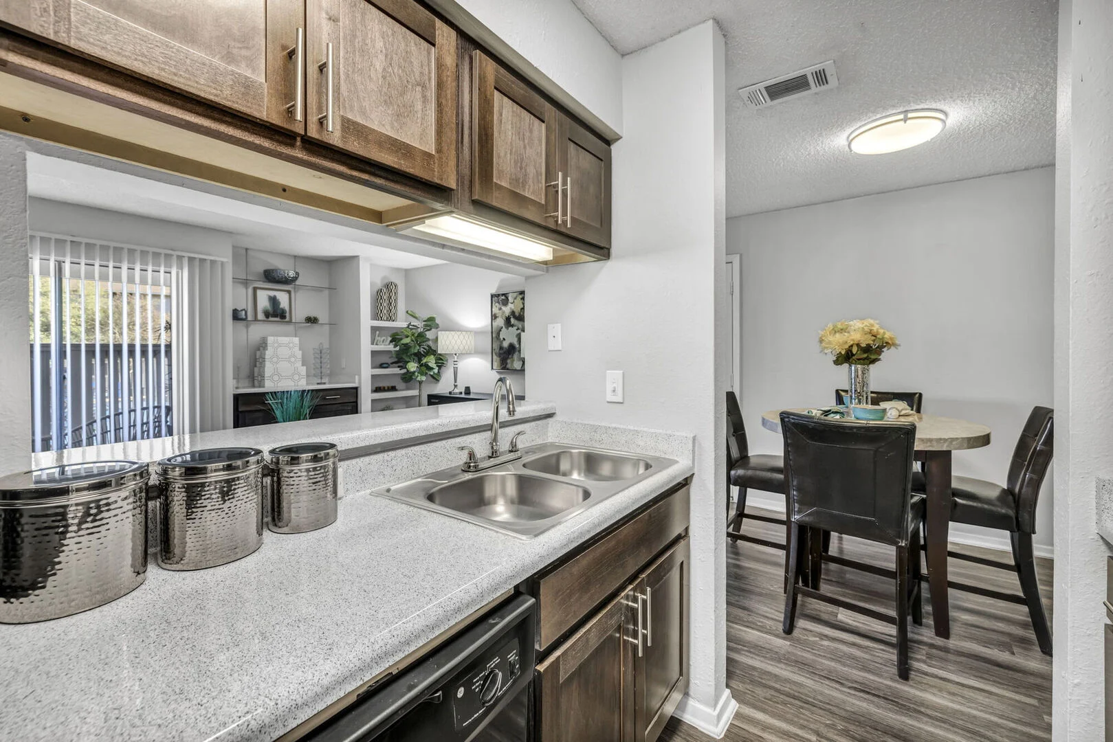 Modern Kitchen in a Contemporary Apartment A modern kitchen featuring dark wood cabinets and a granite countertop, seen from an open layout towards a dining area in the background.
