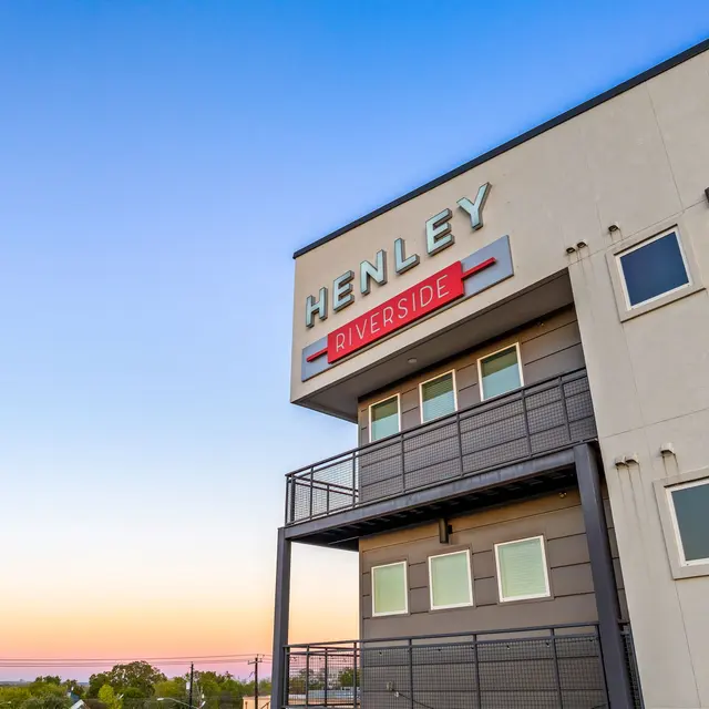 Exterior view of a modern building with a sign that reads 'HENLEY RIVERSIDE' against a clear blue sky during sunset.