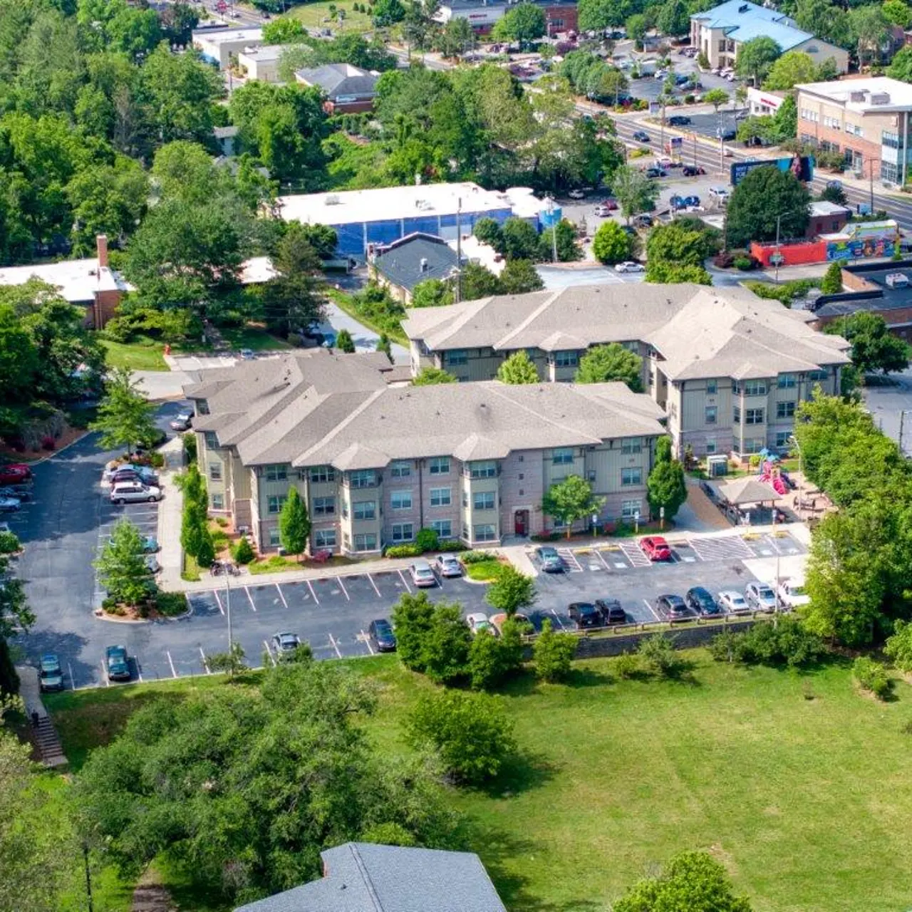 Aerial view of a mid-sized apartment complex surrounded by dense greenery and residential areas.